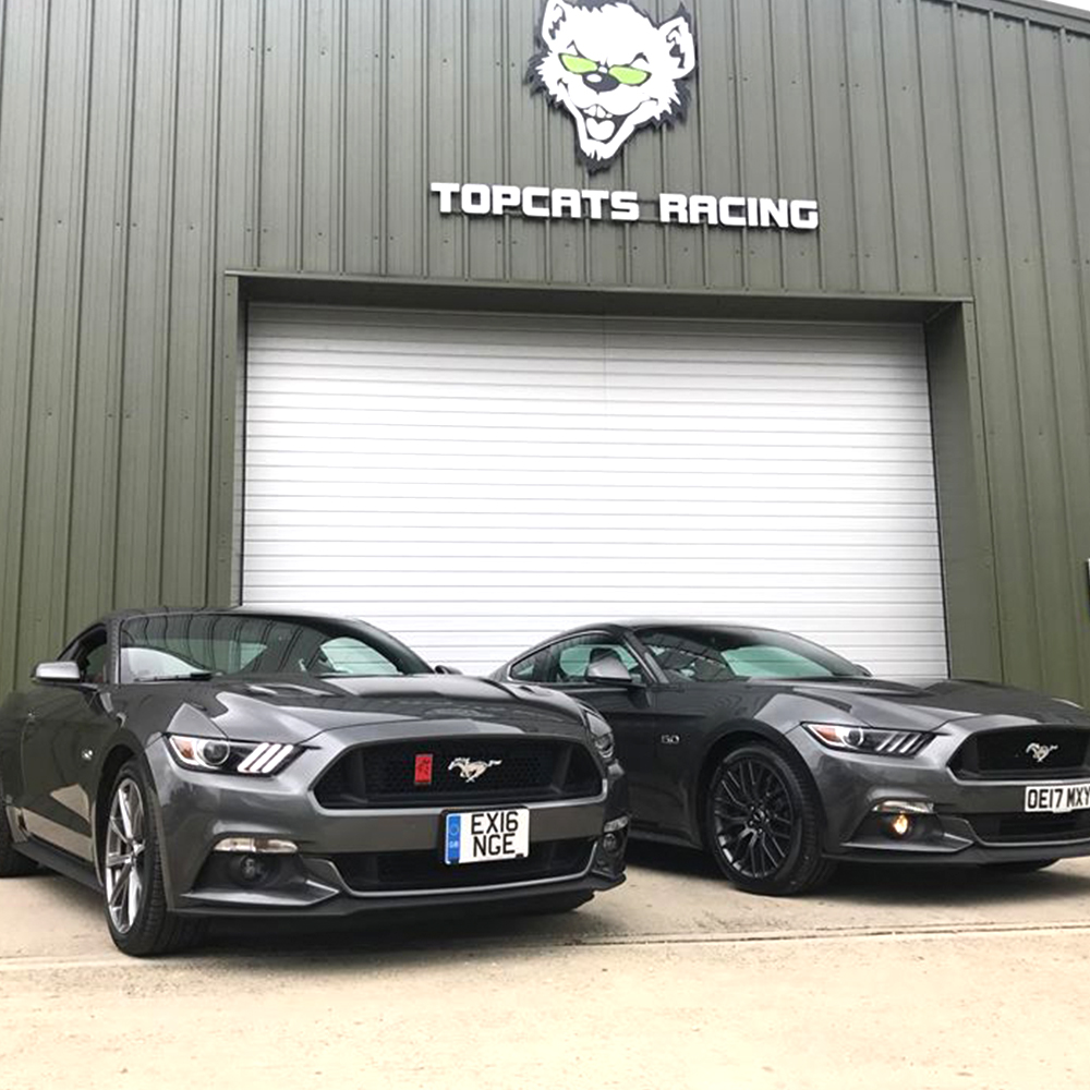 two metallic grey mustangs in front of topcats racing workshop