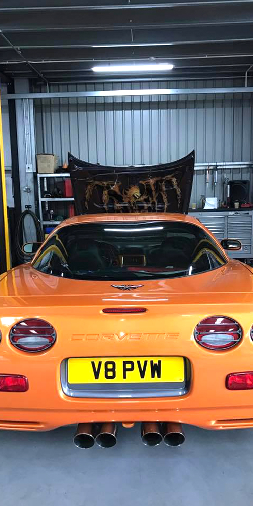 orange corvette rear bumper with bonnet open as topcats racing team work on engine